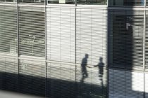 Shadow of two businessmen on a sunblind of building — Stock Photo