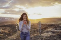 Island, junge Frau nutzt Smartphone bei Sonnenuntergang — Stockfoto