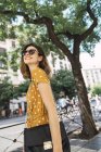 Улыбающаяся женщина в жёлтом платье в горошек и солнечных очках, гуляющая по городу — стоковое фото