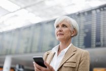 Старша бізнес-леді, що використовує мобільний телефон в аеропорту — стокове фото