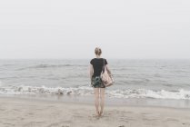Vue arrière de la femme debout sur la plage regardant la distance — Photo de stock