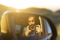Jovem mulher tirando foto de sua imagem de espelho em seu carro — Fotografia de Stock