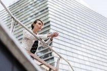 Geschäftsfrau lehnt an Geländer eines Bürogebäudes und blickt in die Ferne — Stockfoto