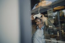 Homme d'affaires mature assis dans un café, regardant à travers des lunettes VR — Photo de stock