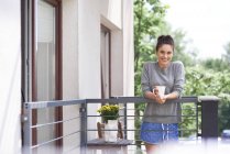 Красива біла жінка з чашкою кави вранці на балконі і дивиться на камеру — стокове фото