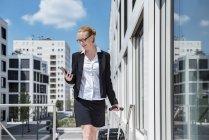 Femme d'affaires souriante avec valise regardant le téléphone portable — Photo de stock