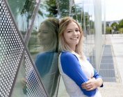 Усміхнена блондинка молода жінка спирається на скляний фасад — стокове фото