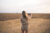 Молода жінка, стоячи в полі, робить смартфон селфі — стокове фото