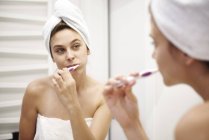 Дзеркальний образ молодої жінки у ванній чищення зубів — стокове фото