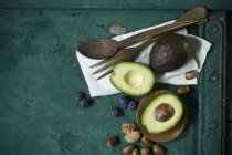 Cloth, salad cutlery, avocados, blueberries and nuts on green ground — Stock Photo