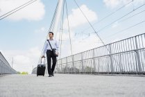 Businessman with rolling suitcase crossing a bridge — Stock Photo