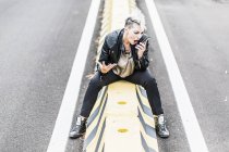 Mujer punk agresiva sentada al borde de la carretera gritando en el teléfono celular - foto de stock