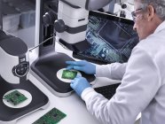 Ingénieur utilisant un stéréomicroscope 3D pour le contrôle de la qualité dans la fabrication de cartes de circuits imprimés pour l'industrie électronique — Photo de stock