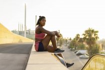 Young woman during workout sitting on wall on street — Stock Photo