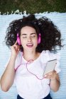 Ritratto di giovane donna sdraiata su coperta ad ascoltare musica con smartphone e cuffie rosa — Foto stock