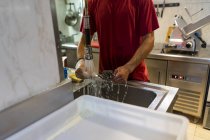 Мужчина стирает столовые приборы над раковиной на кухне ресторана — стоковое фото