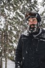 Улыбающийся молодой человек в лыжной одежде в зимнем лесу смотрит боком — стоковое фото