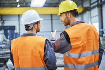 Rear view of men wearing protective workwear talking in factory — Stock Photo
