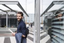Sorrindo jovem empresário de pé ao ar livre segurando jornal — Fotografia de Stock