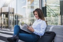 Ritratto di giovane imprenditrice seduta sulla panchina a leggere il giornale — Foto stock