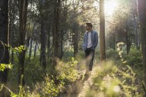 Jovem de pé na floresta, contra o sol — Fotografia de Stock