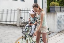 Mother and daughter riding bicycle, daughter wearing helmet, sitting in children seat — Stock Photo