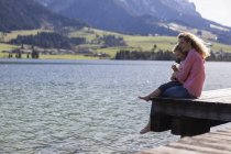 Австрія, Тіроль, Волчзе, щаслива мати й дочка сидять на пристані біля озера. — стокове фото