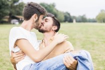 Kissing young gay couple relaxing in park — Stock Photo