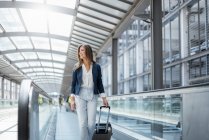 Smiling young businesswoman with baggage on moving walkway — Stock Photo