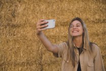 Giovane donna in piedi davanti alle balle di fieno, facendo selfie smartphone — Foto stock