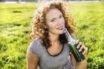 Porträt einer rothaarigen jungen Frau, die auf der grünen Wiese ein Getränk genießt — Stockfoto