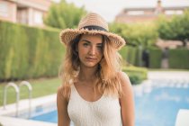 Portrait of young woman with straw hat and swimsuit, pool in background — Stock Photo