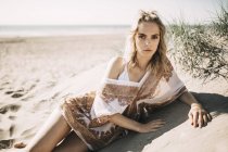 Femme blonde sur la plage, allongé sur une dune de sable et regardant la caméra — Photo de stock