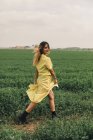 Jeune femme en robe jaune marchant dans le champ vert — Photo de stock