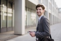 Uomo d'affari sorridente in città con borsa e tablet — Foto stock