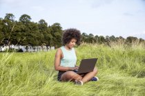 Жінка сидить на галявині і за допомогою ноутбука — стокове фото