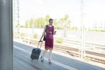 Зріла бізнес-леді зі смартфоном і валіза, що йде на платформі — стокове фото