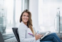 Sonriente joven empresaria sentada en la sala de espera usando tableta - foto de stock