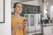 Giovane imprenditore in piedi in caffetteria e utilizzando smartphone — Foto stock