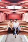 Молодая влюбленная гей-пара сидит на стальных балках пешеходного моста и смотрит друг на друга — стоковое фото