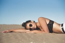 Portrait of teenage girl wearing sunglasses lying on sandy beach — Stock Photo