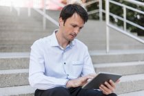Empresário sentado nas escadas usando tablet — Fotografia de Stock
