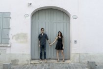 Jovem casal de pé de mãos dadas na frente do edifício — Fotografia de Stock