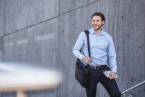 Ritratto di uomo d'affari sorridente con borsa per laptop al muro di cemento — Foto stock