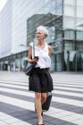 Mujer mayor con teléfono celular y equipaje en movimiento en la ciudad — Stock Photo