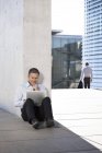 Бизнесмен, опираясь на стену на открытом воздухе, пользуется ноутбуком — стоковое фото