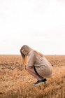 Junge Frau kauert auf Feld — Stockfoto