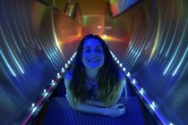 Portrait de jeune femme illuminée bleue sur les marches de l'escalator éclairé — Photo de stock