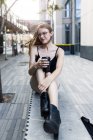 Junge Frau sitzt auf einer Mauer in der Stadt und trinkt Kaffee to go — Stockfoto