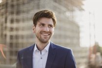 Портрет улыбающегося бизнесмена перед стройкой, смотрящего в сторону — стоковое фото